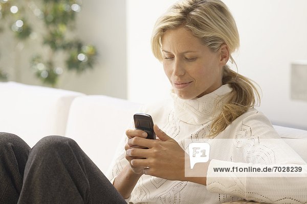 Mid adult woman reading text message on sofa