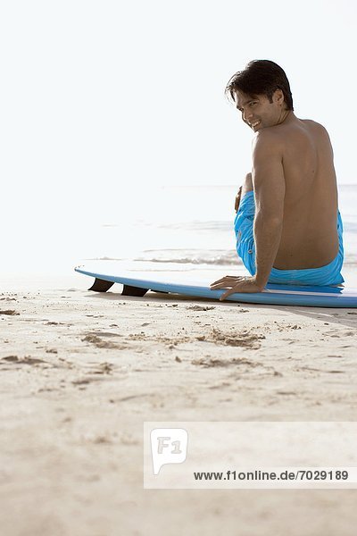 Young man sitting on surfboard on beach