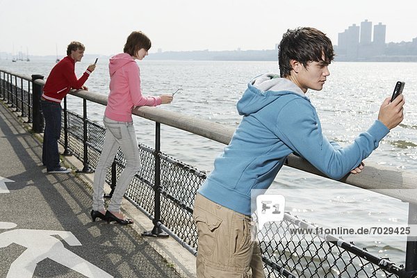 Three teenagers using mobile phone at waterfront