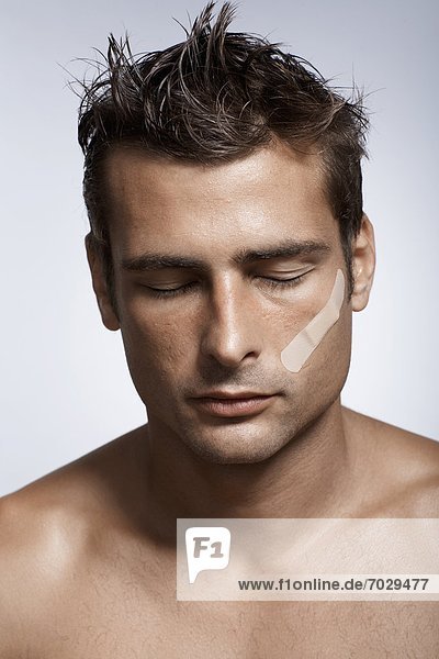 Mid adult man with adhesive plaster on cheek