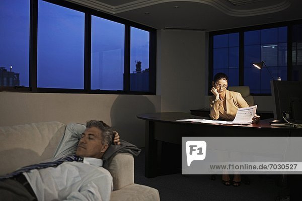 Businesswoman Working Late  Man Sleeping on Sofa in Office