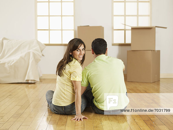 Mid-Adult Couple Sitting on Floor near Cardboard Boxes  Woman Looking Back
