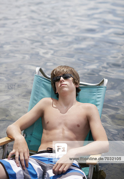 Teenage Boy Relaxing on Lounge Chair by Water