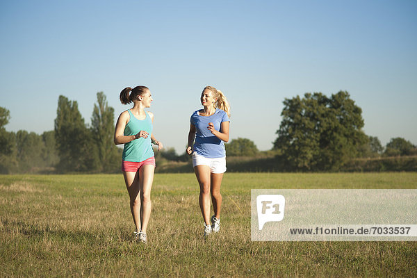Zwei junge Frauen joggen auf einer Wiese