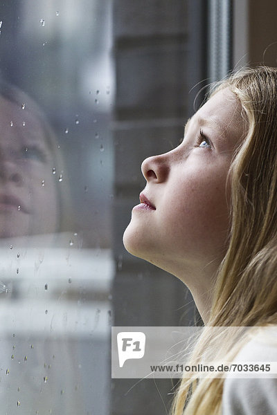 Blond girl looking out of rainy window