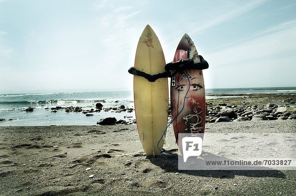 Two People Holding Surfboards In Front Of Them On Beach