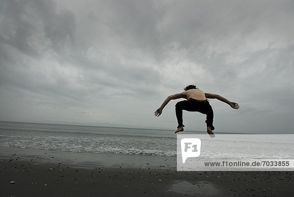 Woman Jumping On Beach Under Cloudy Skies