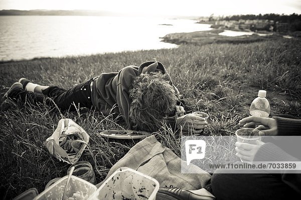 People Relaxing And Eating On Grass Near Waterfront