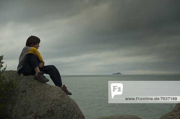 A Boy Sits On A Rock Watching The Ocean