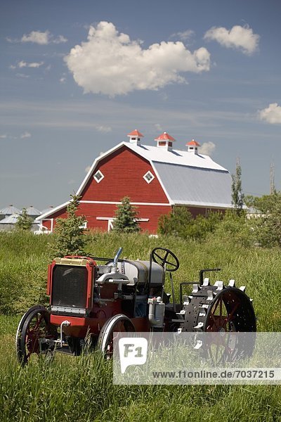 'Old Red Tractor In A Field With A Red Barn In The Background