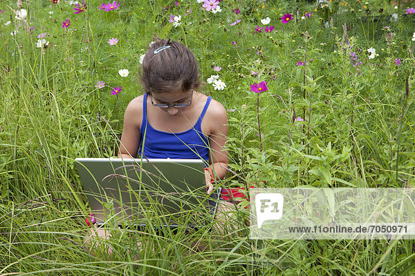 Mädchen  11 Jahre  mit einem Laptop  Notebook  inmitten einer Blumenwiese in freier Natur