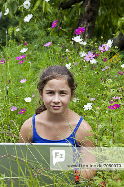 Mädchen  11 Jahre  mit einem Laptop  Notebook  inmitten einer Blumenwiese in freier Natur