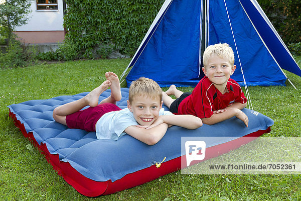 Zwei Jungen auf einer Luftmatratze  beim Zelten im Garten