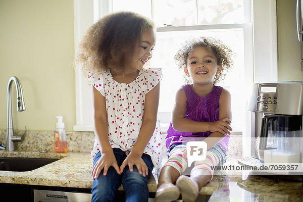 Mixed race sisters sitting on kitchen counter