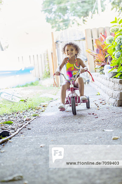 Mixed race girl riding tricycle