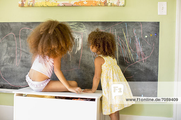 Mixed race girls writing on blackboard