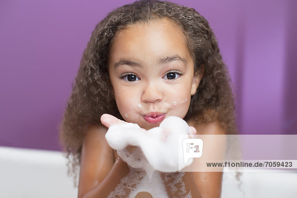 Mixed race girl playing with bubbles in bathtub