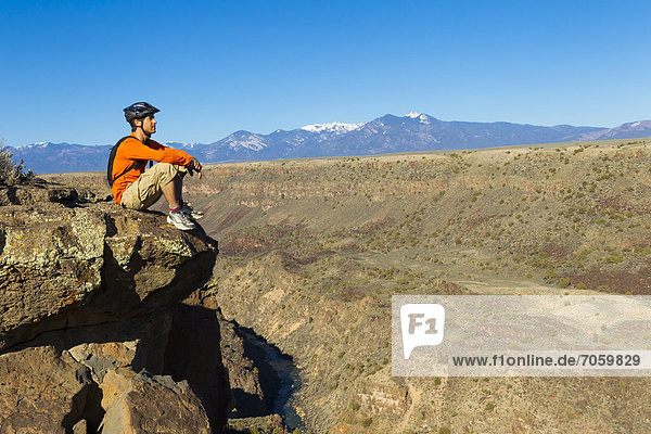 Hispanic man sitting on canyon cliff