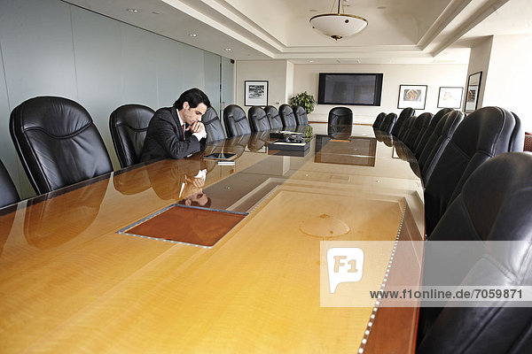 Hispanic businessman sitting in empty conference room