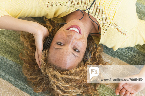 Young woman lying on carpet and listening to music on headphones