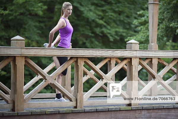 Young woman stretching leg on wooden bridge after running.