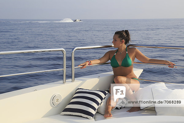 Young woman wearing a green bikini sitting on the sun deck of a motor yacht  French Riviera  Cote d'Azur  Mediterranean Sea  Europe