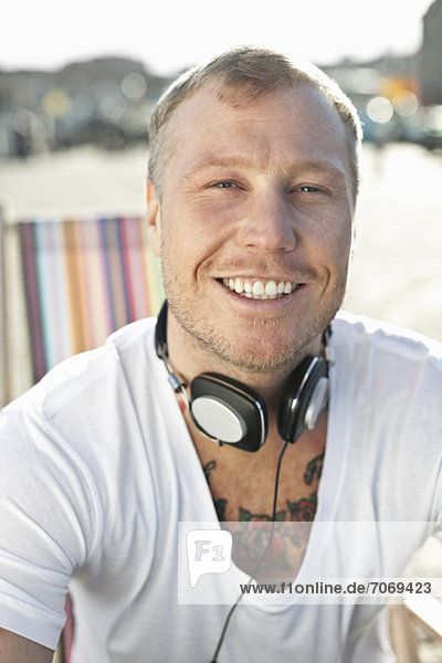 Porträt eines glücklichen Mannes mit Kopfhörern am Strand
