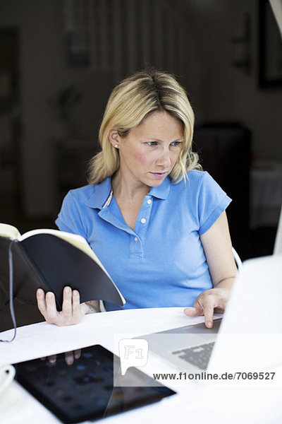 Mittlere erwachsene Frau mit Buch und digitalem Tablett mit Laptop