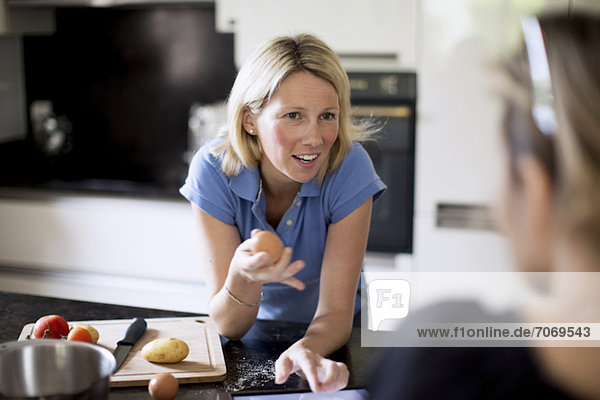 Frau im Gespräch mit Freundin bei der Zubereitung des Essens in der Küche