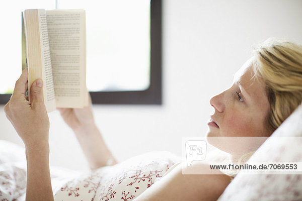 Seriöse erwachsene Frau auf dem Bett liegend und Lesebuch