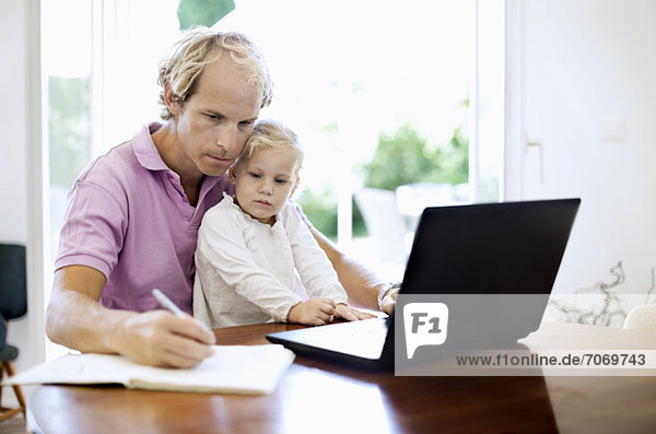 Mid Erwachsene Mann mit Laptop beim Schreiben von Notizen sitzen mit Tochter am Schreibtisch