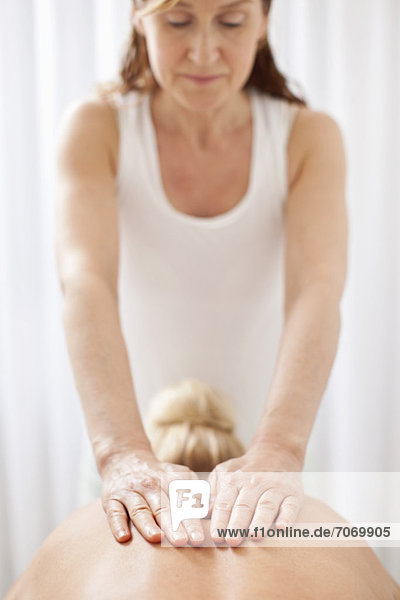 Reife Masseurin massiert den Rücken einer erwachsenen Frau im Wellnessbereich.