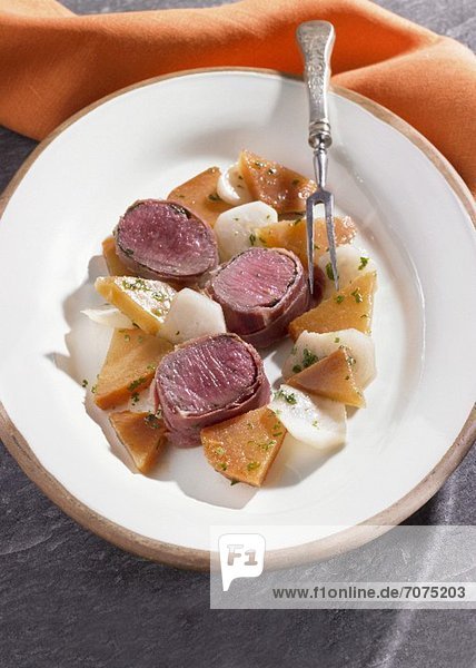 Saddle of lamb wrapped in bacon with yellow and white turnips