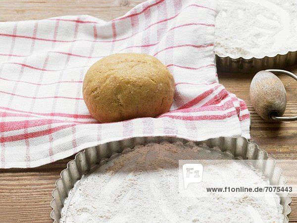 A ball of dough on a tea towel next to a floured quiche dish