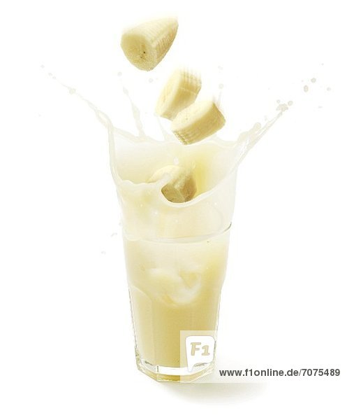 Bananenscheiben fallen in ein Glas mit Bananensaft