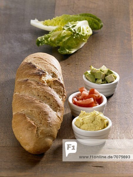 Ingredients for a baguette with an avocado dip (bread  curry dip  tomatoes  avocado and lettuce)