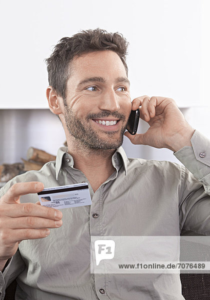 Junger Mann telefoniert mit Handy  Kreditkarte in der Hand