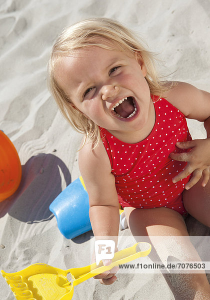 Kleines Mädchen sitzt im Sand und schreit