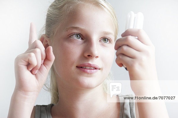 Mädchen hält eine Energiesparlampe in der Hand und meldet sich