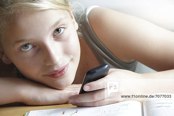 Girl looking at a smartphone with her homework lying in front of her