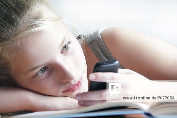 Mädchen schaut auf ein Smartphone und Hausaufgaben liegen davor