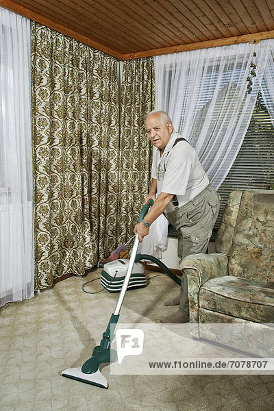 Älterer Mann beim Hausputz mit Staubsauger