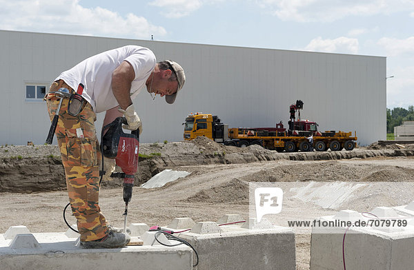 Ein Arbeiter bohrt Löcher in Steinblöcke  die anschließend f¸r eine Baugrund-Probebelastung verwendet werden sollen  auf einer Baustelle in Fridolfing  Bayern  Deutschland  Europa