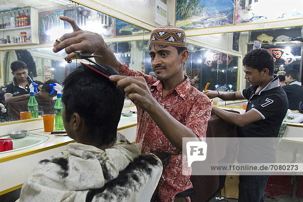 Two hairdressers cut their customer's hair  New Market  Dhaka  Bangladesh  South Asia  Asia