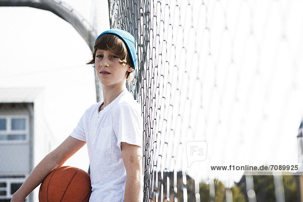 Boy standing with basketball at fence