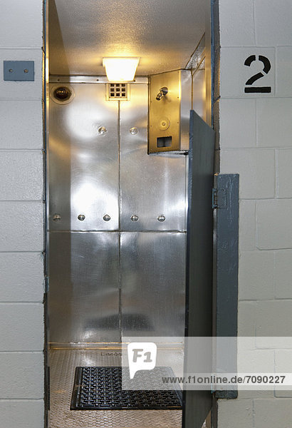 A prisoner shower cubicle at a Correctional Facility. Stainless steel walls and a mat on the floor. Number on the wall. Half door.