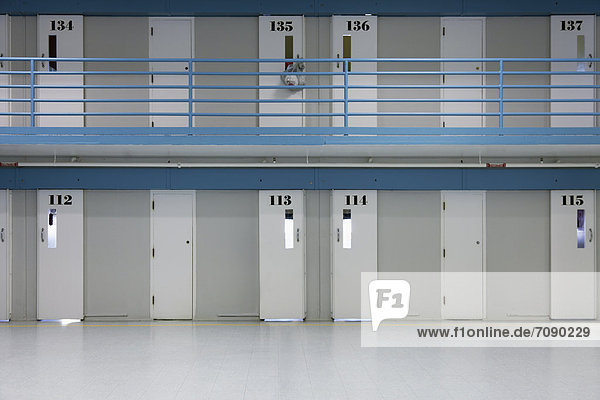Prison cells on two floors. Doors opening on to a landing. Rooms at a Correctional Facility. Numbers and observation hatches.
