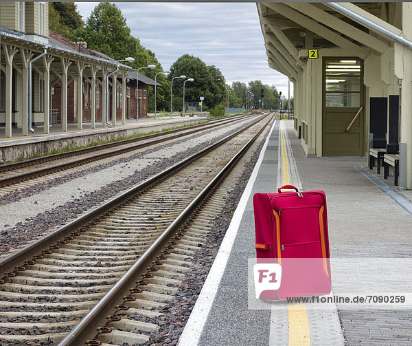 An empty railway station in Estonia. A single red suitcase on the platform beside the tracks.