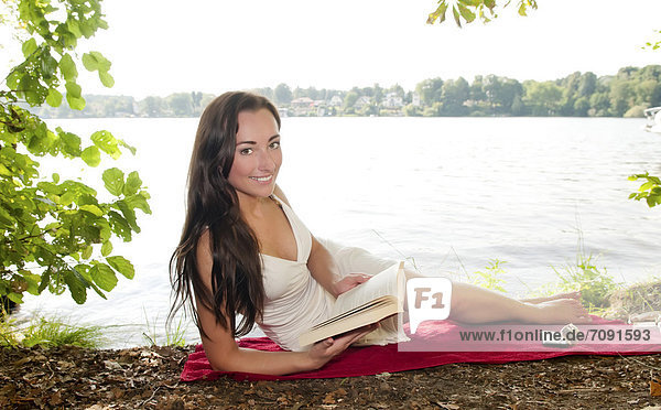 Young woman reading book at lakeshore