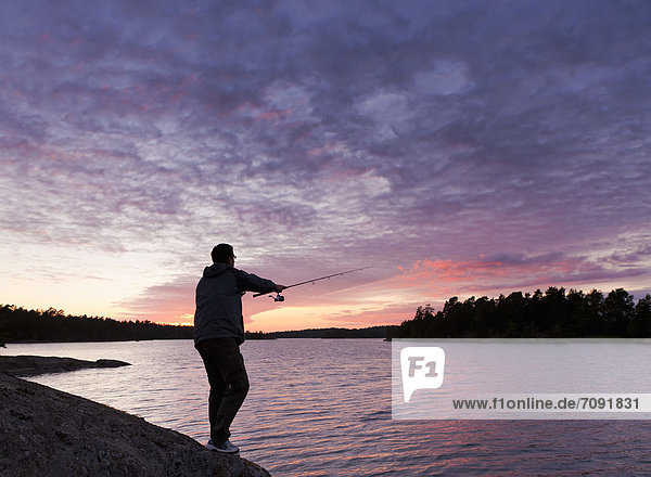 Schweden  Junger Mann beim Fischen bei Sonnenuntergang